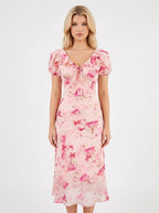 Woman wearing a pink floral print midi dress with short puff sleeves and a tie-front V-neckline, shown from the front.
