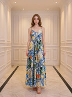 Woman wearing a long, sleeveless maxi dress with a colorful fruit and floral print, standing in a hallway.