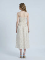 Back view of a woman wearing a white floral print midi dress with spaghetti straps and a square neckline, standing against a white background.