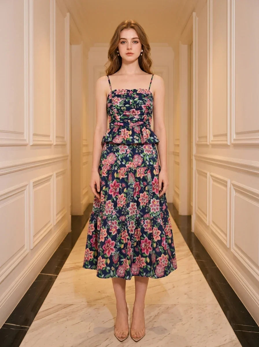 Woman standing in a hallway wearing a navy floral print midi dress with spaghetti straps and a peplum waist.