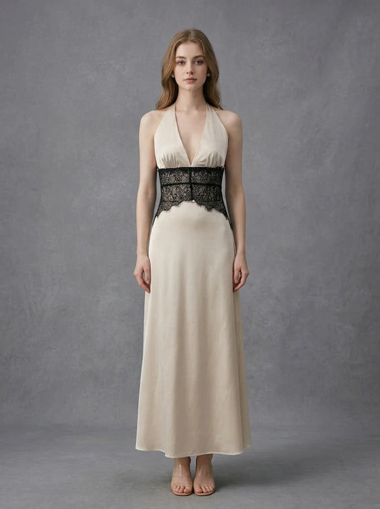 Woman in a cream satin maxi dress with black lace waist detail, standing against a grey backdrop.