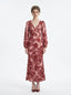 woman wearing a pink and red floral print satin maxi wrap dress with long bishop sleeves and a v-neck, standing against a white background