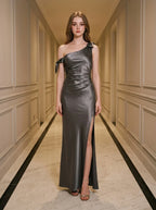 Woman wearing a floor-length grey satin one-shoulder dress with a high slit and bow accents, standing in a hallway.