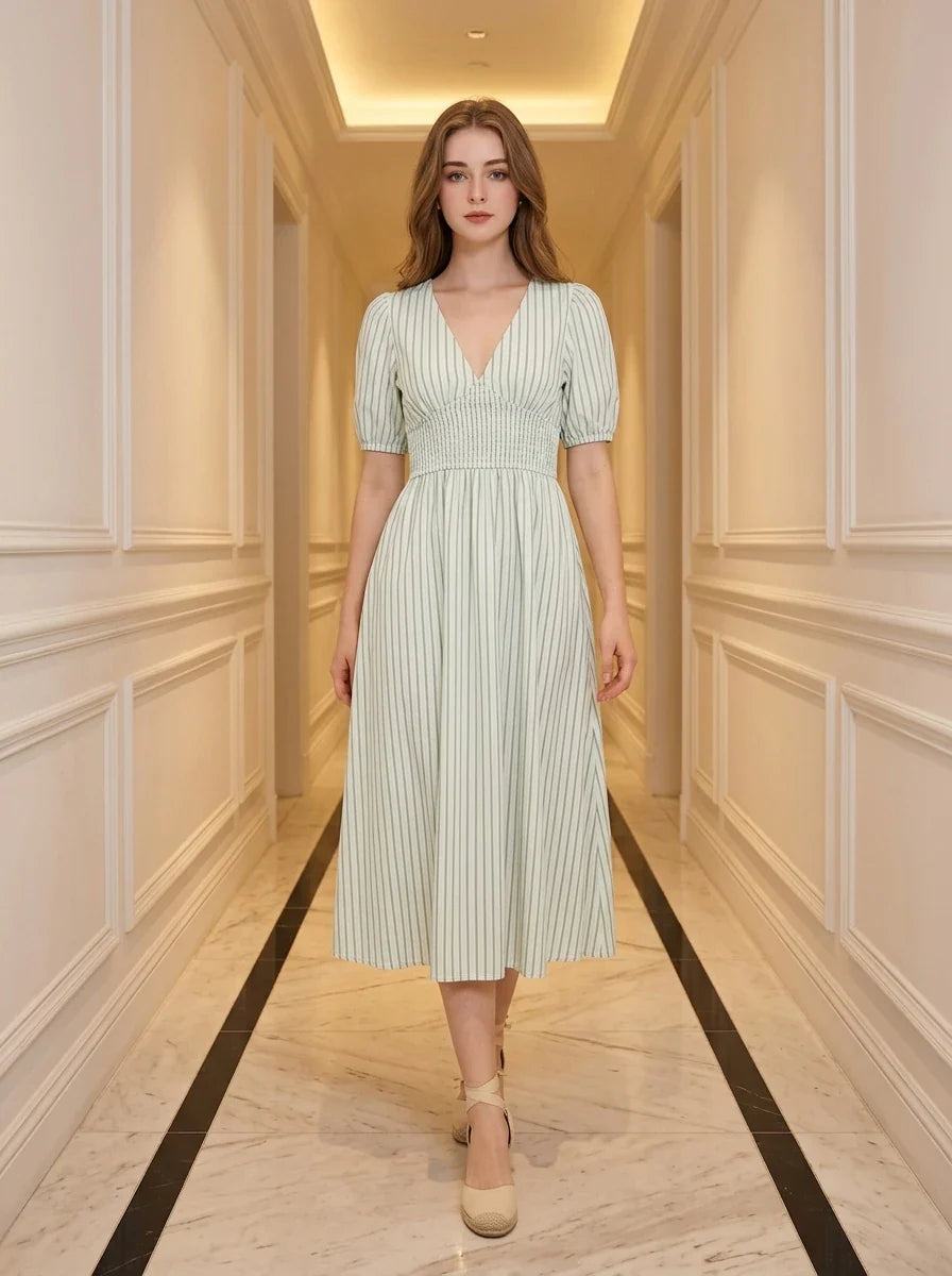 Woman standing in a hallway wearing a light green and white striped midi dress with puff sleeves and a V-neck.