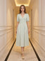 Woman standing in a hallway wearing a light green and white striped midi dress with puff sleeves and a V-neck.