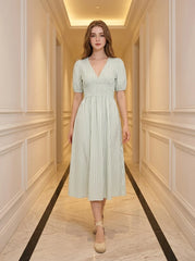 Woman standing in a hallway wearing a light green and white striped midi dress with puff sleeves and a V-neck.