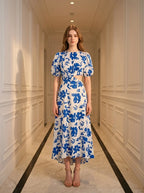 Woman wearing a white and blue floral print midi dress with cut-out waist and puff sleeves, standing in a hallway.