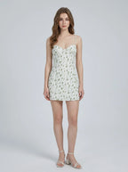 Woman wearing a white floral print mini dress with spaghetti straps and a sweetheart neckline, standing against a white background.
