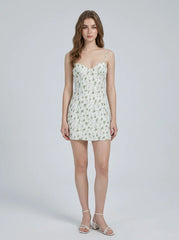 Woman wearing a white floral print mini dress with spaghetti straps and a sweetheart neckline, standing against a white background.