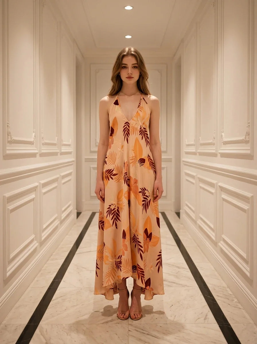 Woman standing in a hallway wearing a long, floral print, halter neck dress with an open back.