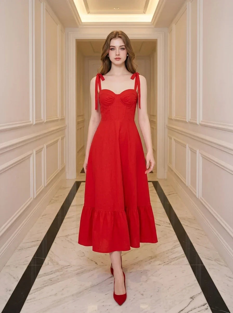 Woman wearing a red midi dress with tie straps and ruffle hem, standing in a hallway.