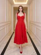 Woman wearing a red midi dress with tie straps and ruffle hem, standing in a hallway.