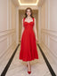 Woman wearing a red midi dress with tie straps and ruffle hem, standing in a hallway.