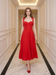 Woman wearing a red midi dress with tie straps and ruffle hem, standing in a hallway.
