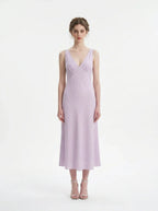 Model wearing a lavender midi dress with a V-neckline and sleeveless design, standing against a white background.