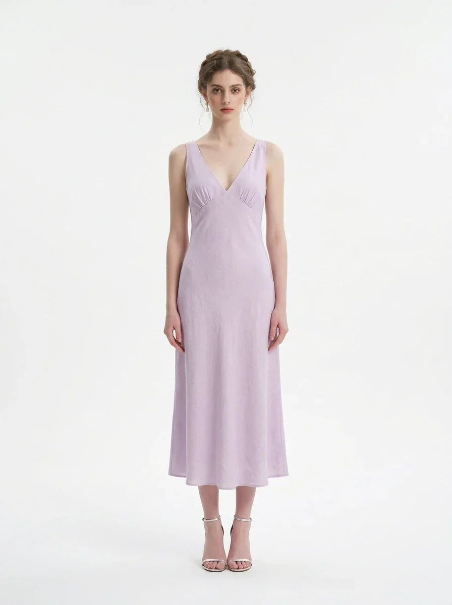 Model wearing a lavender midi dress with a V-neckline and sleeveless design, standing against a white background.