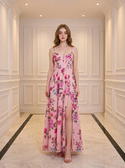 Woman wearing a pink floral print maxi dress with spaghetti straps and a high slit, standing in a hallway.