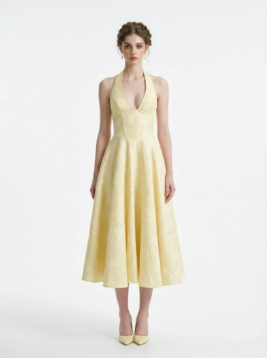 Woman wearing a yellow halter neck midi dress with a full skirt, standing against a white background.