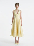 Woman wearing a yellow halter neck midi dress with a full skirt, standing against a white background.