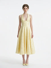 Woman wearing a yellow halter neck midi dress with a full skirt, standing against a white background.