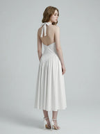 Back view of a woman in a white halter neck midi dress, showing the open back and tie closure.