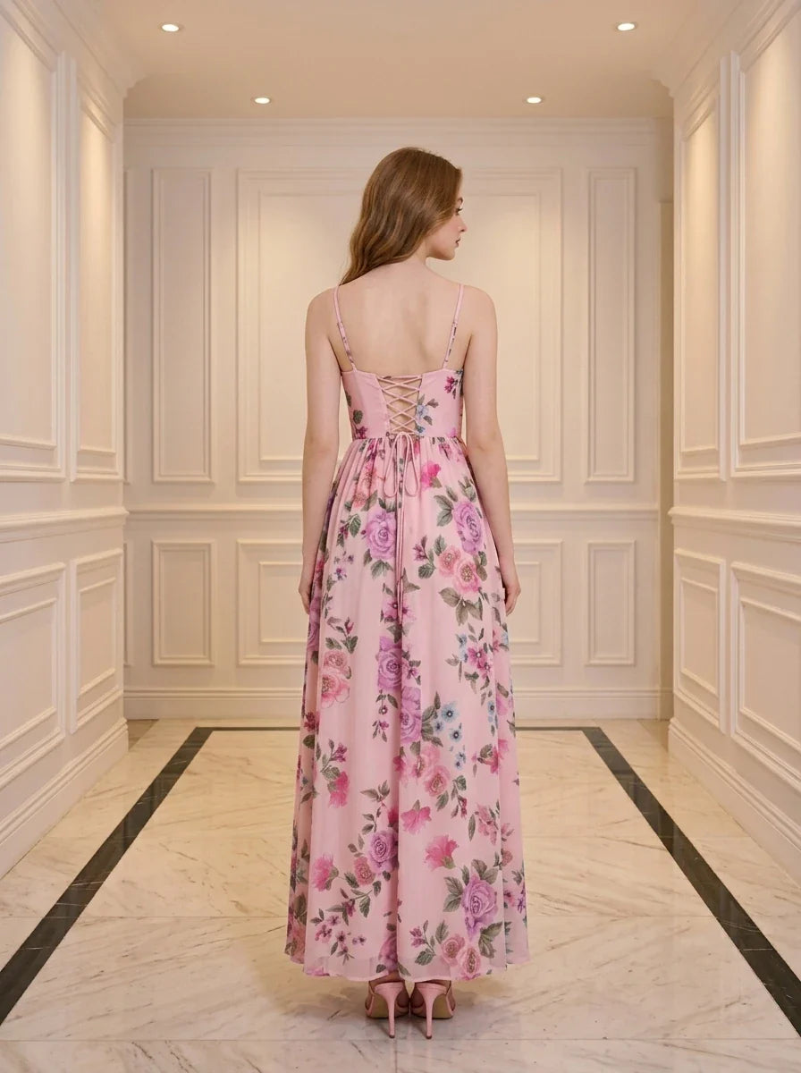 Back view of a woman in a pink floral print maxi dress with spaghetti straps and a lace-up back, standing in a hallway.