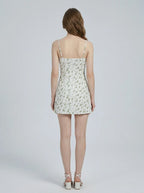 Back view of a woman wearing a white floral print mini dress with spaghetti straps and a sweetheart neckline, standing against a white background.
