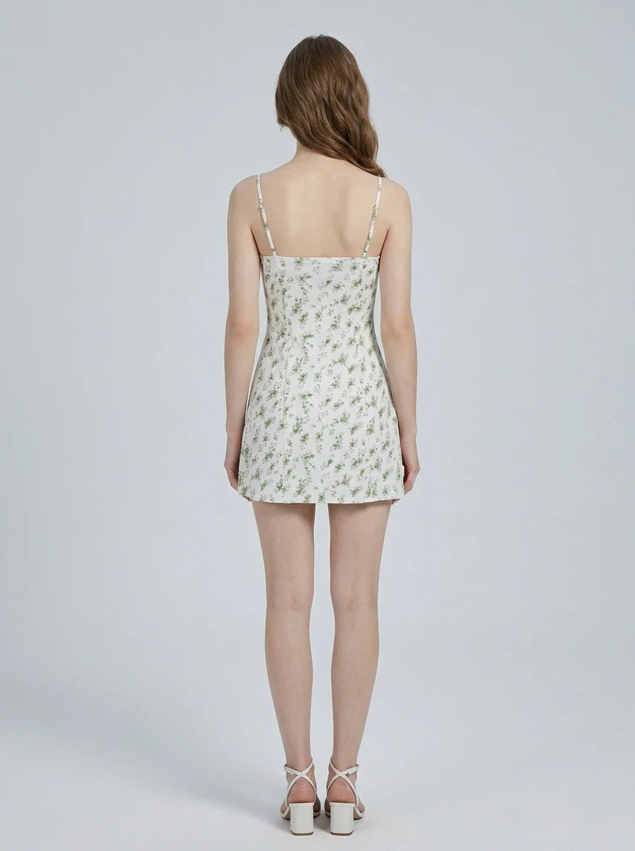 Back view of a woman wearing a white floral print mini dress with spaghetti straps and a sweetheart neckline, standing against a white background.