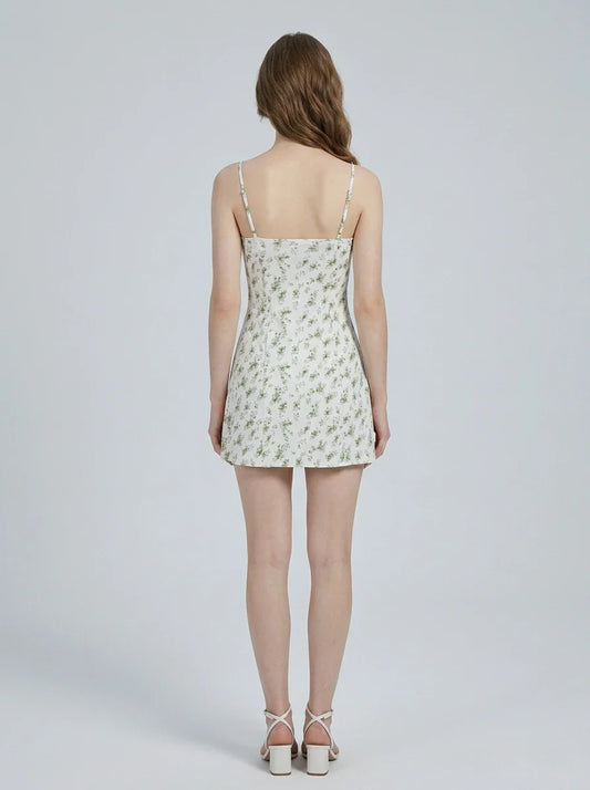 Back view of a woman wearing a white floral print mini dress with spaghetti straps and a sweetheart neckline, standing against a white background.