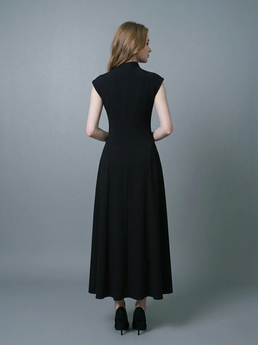 Back view of a woman in a black mock neck cap sleeve A-line dress standing against a grey background.