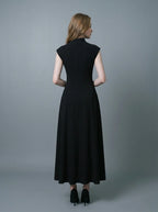 Back view of a woman in a black mock neck cap sleeve A-line dress standing against a grey background.