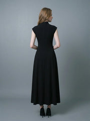 Back view of a woman in a black mock neck cap sleeve A-line dress standing against a grey background.