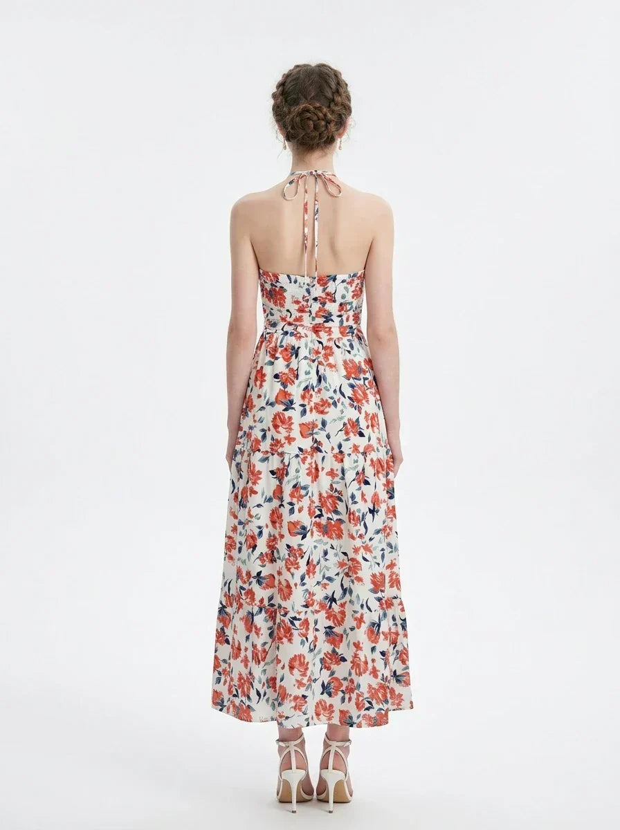 Back view of a woman wearing a white floral print maxi dress with a halter neckline and tiered skirt, standing against a white background.