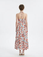 Back view of a woman wearing a white floral print maxi dress with a halter neckline and tiered skirt, standing against a white background.
