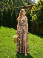 Woman standing on a lawn wearing a floral print maxi dress with a high slit and carrying a straw bag