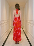 Back view of a woman in a red and pink tropical print halter maxi dress