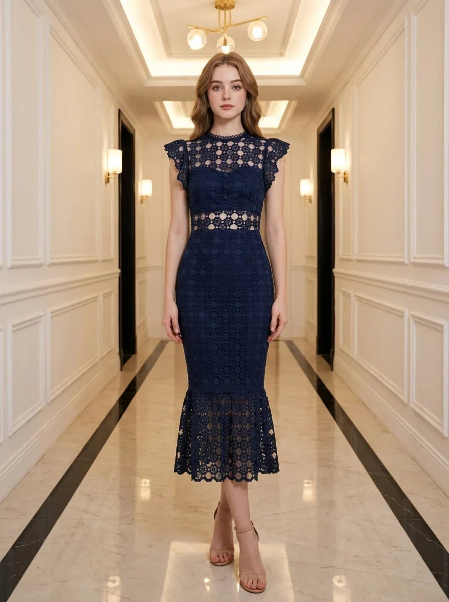 Woman wearing a navy blue lace mermaid dress with a high neck and cap sleeves, standing in a hallway.