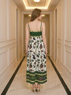 Rear view of a woman in a floral and bird print midi dress with spaghetti straps and a square neckline.
