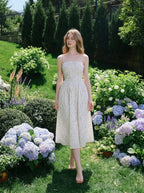 Woman wearing a white floral print midi dress with spaghetti straps and a square neckline, walking in a garden with hydrangeas.