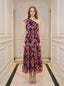 Woman wearing a navy floral print one-shoulder dress with a tiered skirt and ruffle detail, standing in a hallway.