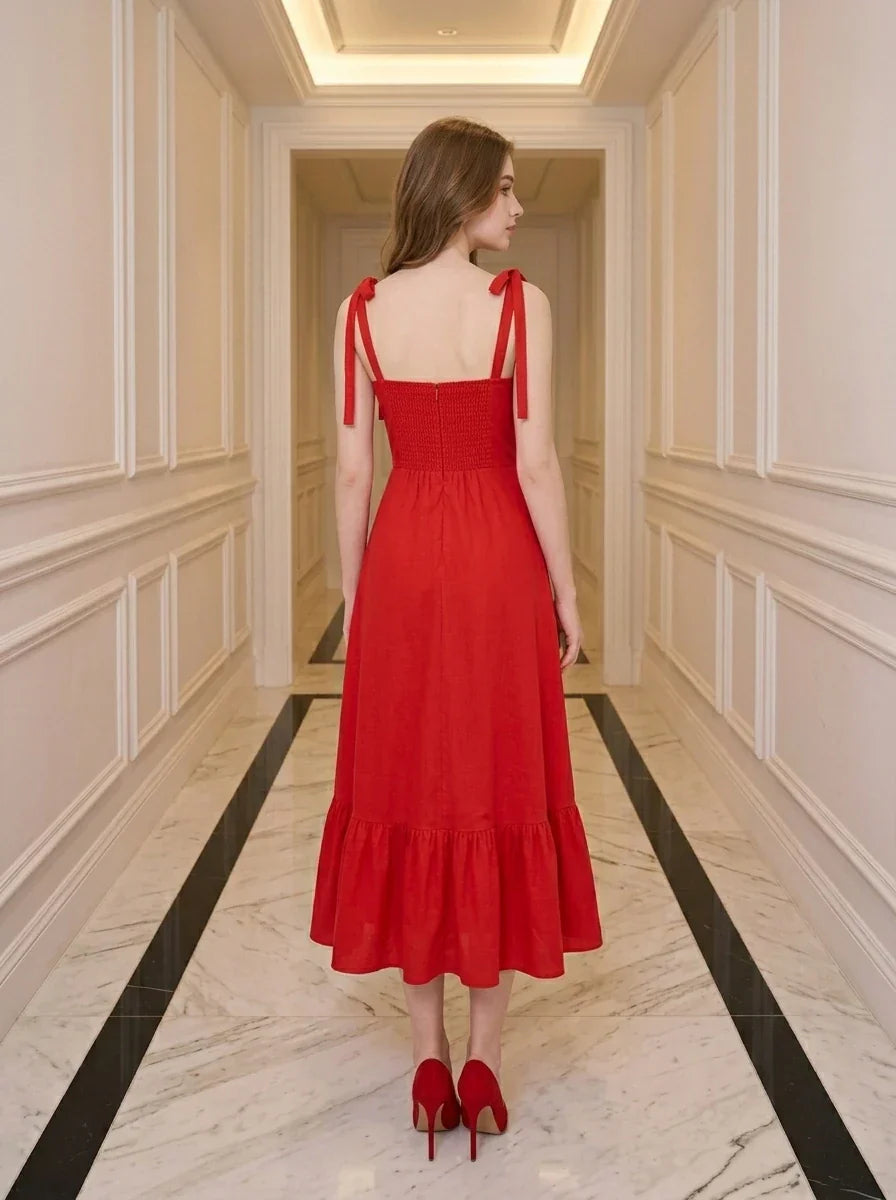 Back view of a woman in a red midi dress with tie straps and ruffle hem, standing in a hallway.