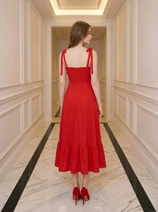 Back view of a woman in a red midi dress with tie straps and ruffle hem, standing in a hallway.