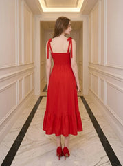 Back view of a woman in a red midi dress with tie straps and ruffle hem, standing in a hallway.