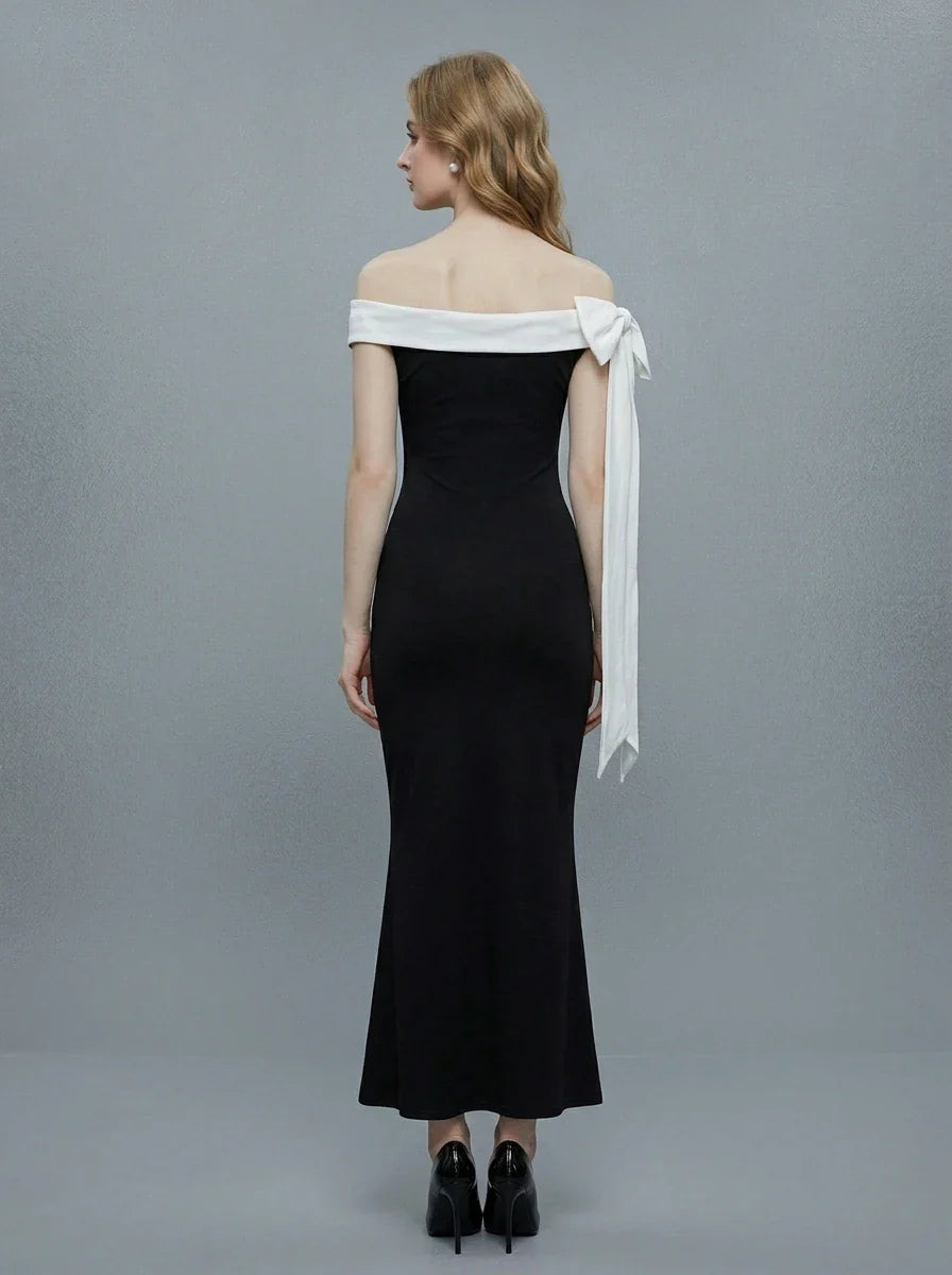 Rear view of a woman in a black off-the-shoulder mermaid gown with a white sash and bow detail.