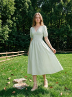 Woman standing in a grassy field wearing a light green and white striped midi dress with puff sleeves and a V-neck.