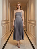 Woman wearing a grey satin midi dress with spaghetti straps and a square neckline, standing in a hallway.