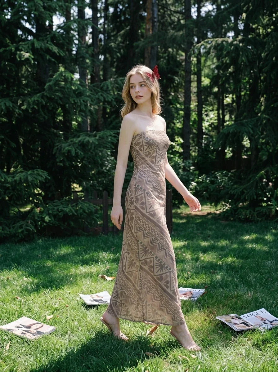 Woman wearing a strapless, patterned maxi dress walking on grass in a wooded area.