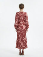 back view of a woman wearing a pink and red floral print satin maxi wrap dress with long bishop sleeves and a v-neck, standing against a white background