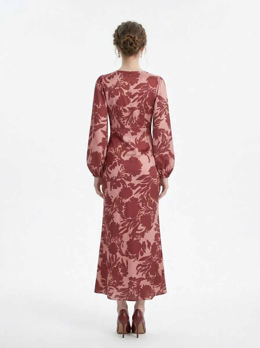back view of a woman wearing a pink and red floral print satin maxi wrap dress with long bishop sleeves and a v-neck, standing against a white background