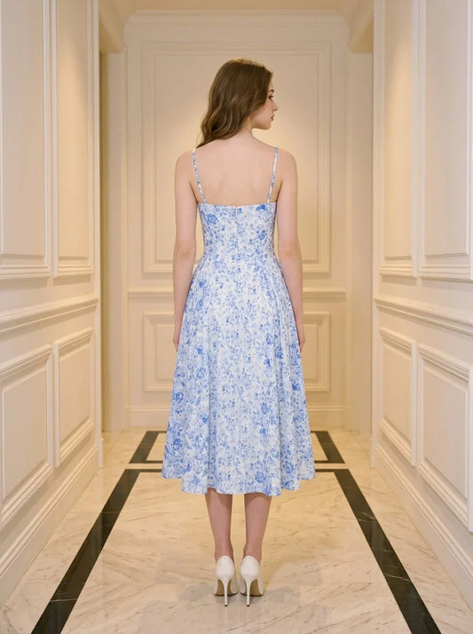 Back view of a woman in a blue and white floral print midi dress with spaghetti straps, standing in a hallway.